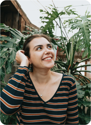 Teenage girl looks up and smiles while standing in front of a plant