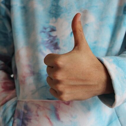 Child in a tie dye shirt, giving a thumbs up