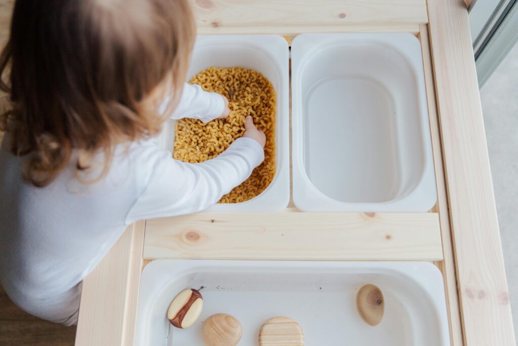Curious autistic child engaging in sensory play with pasta, exploring textures indoors. Curious autistic child engaging in sensory play with pasta, exploring textures indoors.