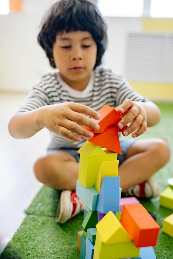 A young child intently assembles a colorful tower of blocks in a classroom setting, showing creativity and focus.
