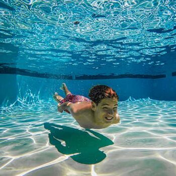 A boy enjoying an underwater swim in a brightly lit swimming pool.